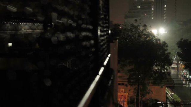 Night rain in Bangkok. View on wet street from balcony through rabitz net. Thailand.