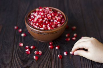 ruby pomegranate seeds in a bowl on a wooden table, a hand reaches out to pomegranate seeds