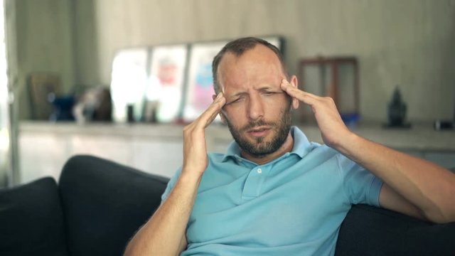 Young man having head pain sitting on sofa in kitchen at home
