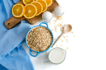 Oat flakes plate with milk, orange, eggs on a wooden white table. Top view of healthy oat flakes breakfast. Copy space. blue napkin Breakfast in bed plate, breakfast table buffet. Healthy ingredients.