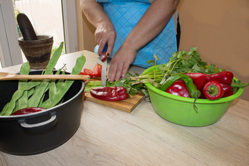 Chef cuts the vegetables into a meal. Preparing dishes. A woman uses a knife and cooks. Woman's hands cooking healthy meal in the kitchen, behind fresh vegetables