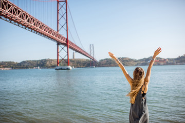 Fototapeta na wymiar Woman enjoying beautiful landscape view on the famous iron bridge standing back near the river in Lisbon, Portugal