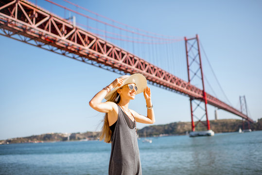 Portrait of a young woman tourist in front of the famous iron bridge traveling in Lisbon city, Portugal