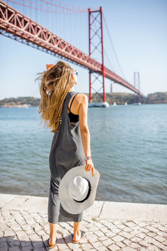 Woman enjoying beautiful landscape view on the famous iron bridge standing back near the river in Lisbon, Portugal