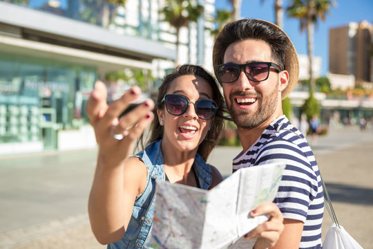 Happy couple in sunglasses holding map laughing