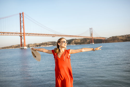Woman having fun standing on the riverside with beautiful view on the iron bridge traveling in Lisbon city, Portugal