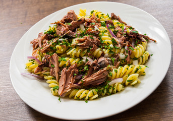 pasta fusilli salad with tuna and onion in white plate on a wooden background
