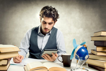 Young adult reading an ebook over a desk full of books and various objects