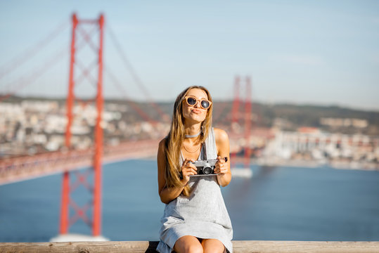 Portrait of a young and cute woman with photo camera on the landscape view background with beautiful iron bridge traveling in Lisbon city, Portugal