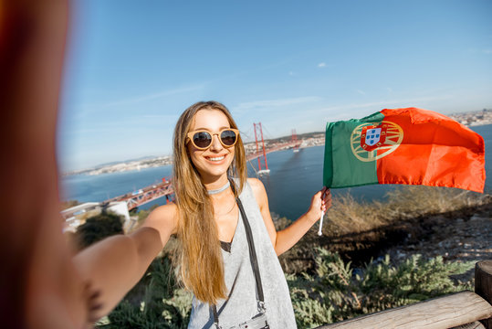 Young woman making selfie photo with portuguese flag on the beautiful landscape view background with bridge and river in Lisbon, Portugal