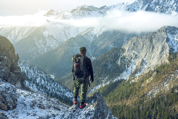 Man hiker with backpack on top of the mountain back, looking at the snow slope. Concept motivation and goal achievement