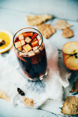Hot mulled wine in a glass with orange slices, anise and cinnamon sticks, star cookies on vintage wood table. Christmas or winter warming drink with recipe ingredients around