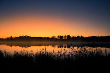 Obraz premium A beautiful sunrise on a lake with a raising mist. Beautiful morning in wetlands in Latvia. Autumn landscape in bright colors.