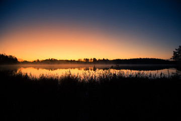 Fototapeta premium A beautiful sunrise on a lake with a raising mist. Beautiful morning in wetlands in Latvia. Autumn landscape in bright colors.