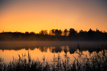 A beautiful sunrise on a lake with a raising mist. Beautiful morning in wetlands in Latvia. Autumn landscape in bright colors.