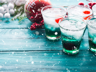 Christmas holiday party background with green alcohol drinks with cherry. Festive aperitif shots and ornaments on wooden dark table