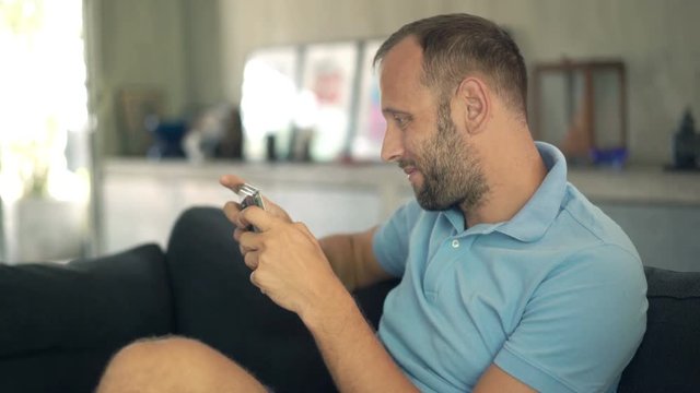 Happy, young man playing game on smartphone on sofa at home

