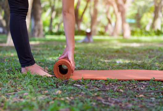 Cropped image of young woman rolling a yoga mat after workout in the morning park