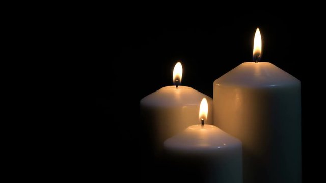 Three white candles burning on black background. 4k shot at 60 fps.
