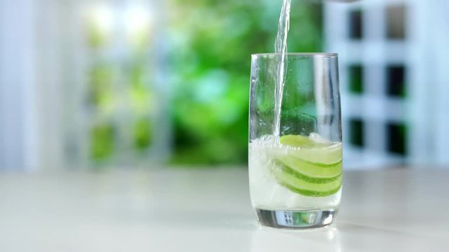 A refreshing drink being poured into a glass with ice, lemon and lime