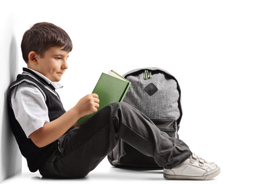 Little schoolboy seated on the floor reading a book