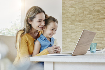 Happy mother with daughter at home looking at laptop