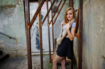 Fototapeta na wymiar Young blonde girl in black skirt with scarf posed at street of city near the iron armor.