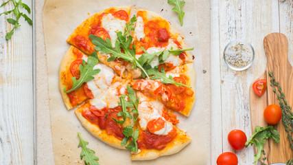 Neapolitan pizza with tomatoes, mozzarella, arugula on a light stone and a wooden background. Mmm, yummy.) Flat lay, top view. Food photo with hands.