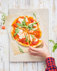 Neapolitan pizza with tomatoes, mozzarella, arugula on a light stone and a wooden background. Mmm, yummy.) Flat lay, top view. Food photo with hands.