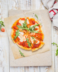 Neapolitan pizza with tomatoes, mozzarella, arugula on a light stone and a wooden background. Mmm, yummy.) Flat lay, top view. Food photo with hands.