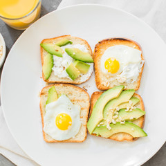 Breakfast. Eggs on toast with avocado, soft white cheese, spices and nuts. White plate, gray concrete background.