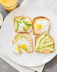 Breakfast. Eggs on toast with avocado, soft white cheese, spices and nuts. White plate, gray concrete background.