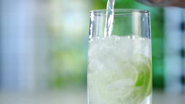 A refreshing drink being poured into a glass with ice, lemon and lime