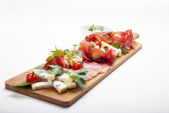 Antipasto platter cold meat plate with grissini bread sticks, prosciutto, slices ham, beef jerky, meats, sausages, salami, ham, olives, laid and arugula on cutting board on wooden background. 