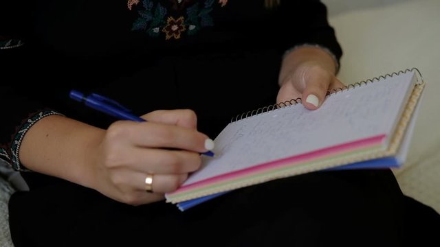 Female hands write a letter holding a notebook on their lap. Woman sits and writes a note with a pen on paper with springs, which is held in air.