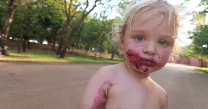 Zombie-like Infant Toddler Boy Walking Towards Camera Wanting To Touch It. Infant Toddler Looking Like A Living Dead Character Walking Forward Towards Camera. Baby Boy Tainted With Red Color In Mouth 