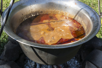 Pot goulash cooked over a fireplace on a tripod.