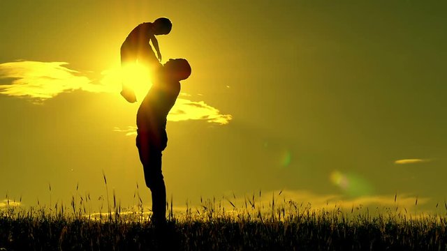 Silhouette of man and child on sunset background. The father holds the son of his son's son and kisses him at a slow pace