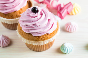 Closeup of cupcakes with vanilla, berries, pink and white cream, chocolate and sprinkles on wooden background. Selective focus. Sweet dessert tasty food concept muffin
