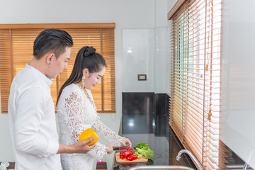 young asian couple cooking together with love,she is cutting vegetable he hug from back