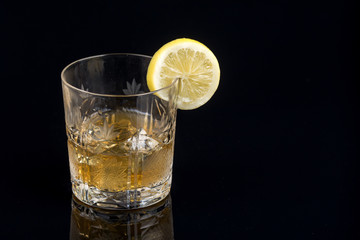 Glass with alcohol drink and lemon on the black background with reflections