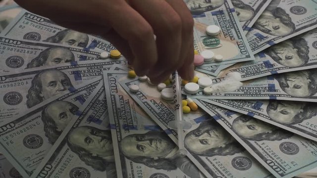 Pills, ampoules, narcotics and syringes rotating on money - healthcare cost concept and drugs addiction