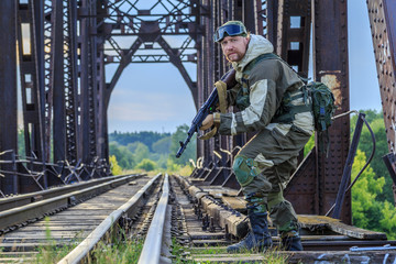 Soldier in uniform, on duty at the railway bridge near the rail with automatic weapons