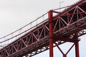 Close-up of red steel beam suspension bridge against grey sky