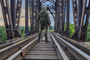 Soldier in uniform on a railway bridge between the rails with automatic weapons