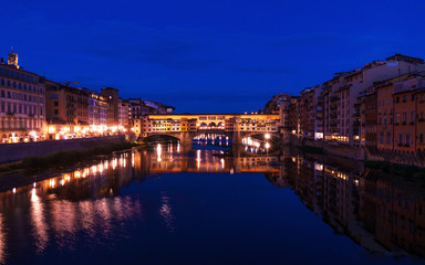Obraz premium Ponte Vecchio bridge in Florence at night time with city lights reflecting in Arno river.