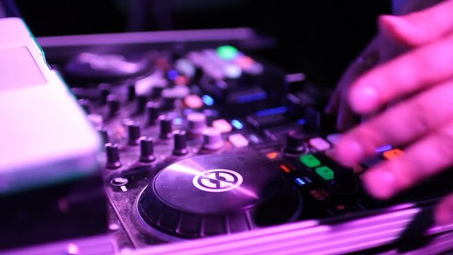 Hands of DJ tweak various track controls on dj's deck.
