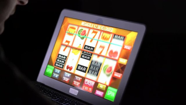 Gambling addicted man in front of online casino slot machine on laptop computer at night - loosing his money. Dramatic low light grain shot.