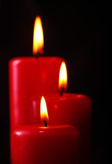 Closeup of three red burning candles against black background .Closeup .Copy space