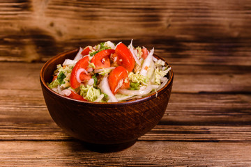 Dietary salad with the chinese cabbage and tomatoes in ceramic bowl on a wooden table